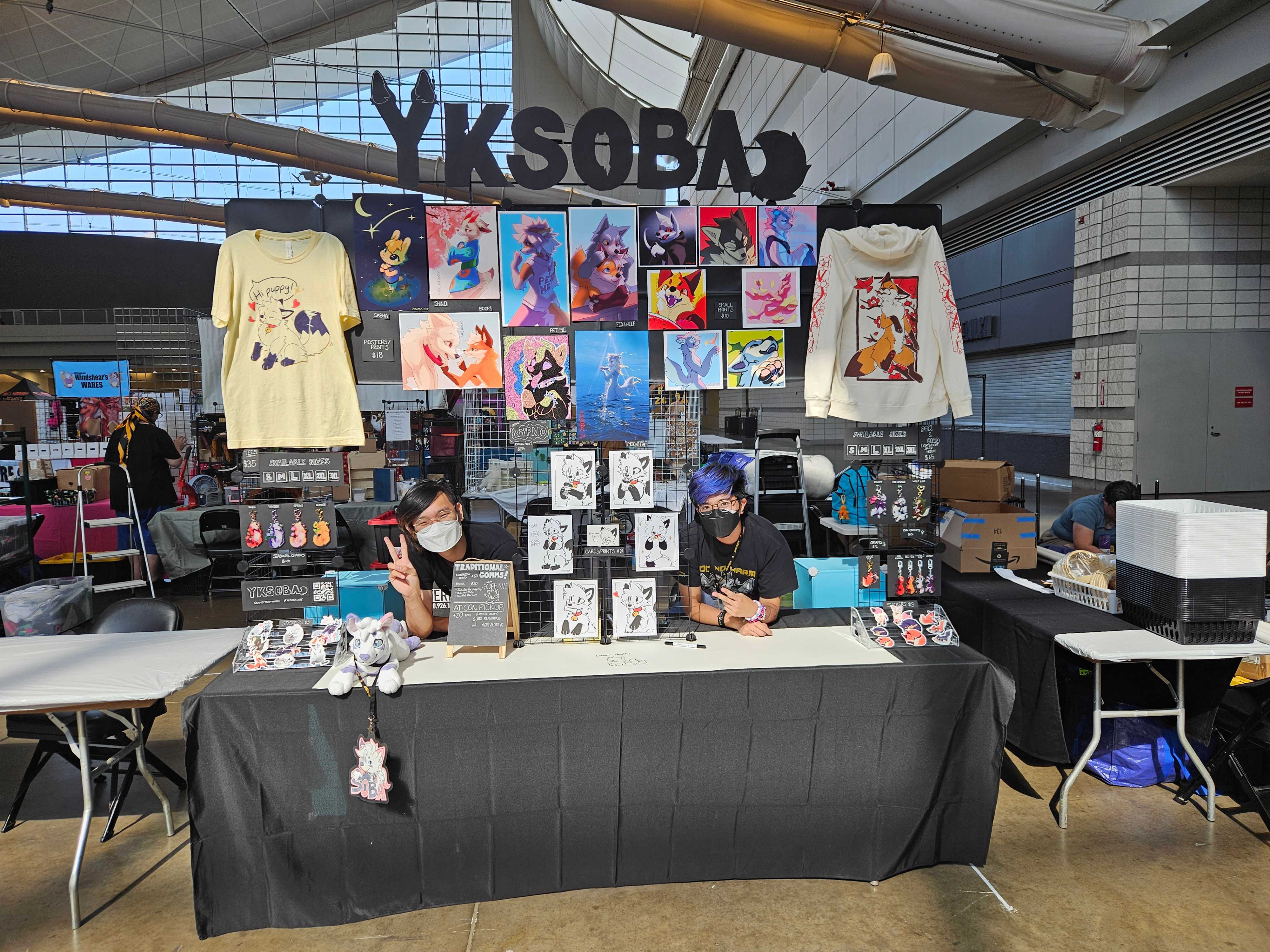 Soba (me) and Rye (my partner) behind the table at Anthrocon '25